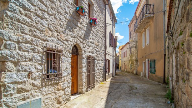 Una estrecha calle empedrada con edificios a ambos lados, que presentan puertas y ventanas de arco con rejas de metal.