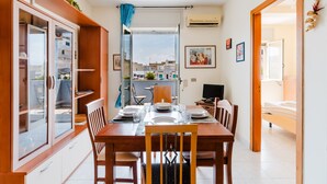 Un comedor con una mesa de madera dispuesta para cuatro, una cocina al fondo y vistas a través de un puerta abierta.