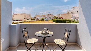 Un balcón con dos sillas y una mesa, vista a una zona residencial y cielo despejado.