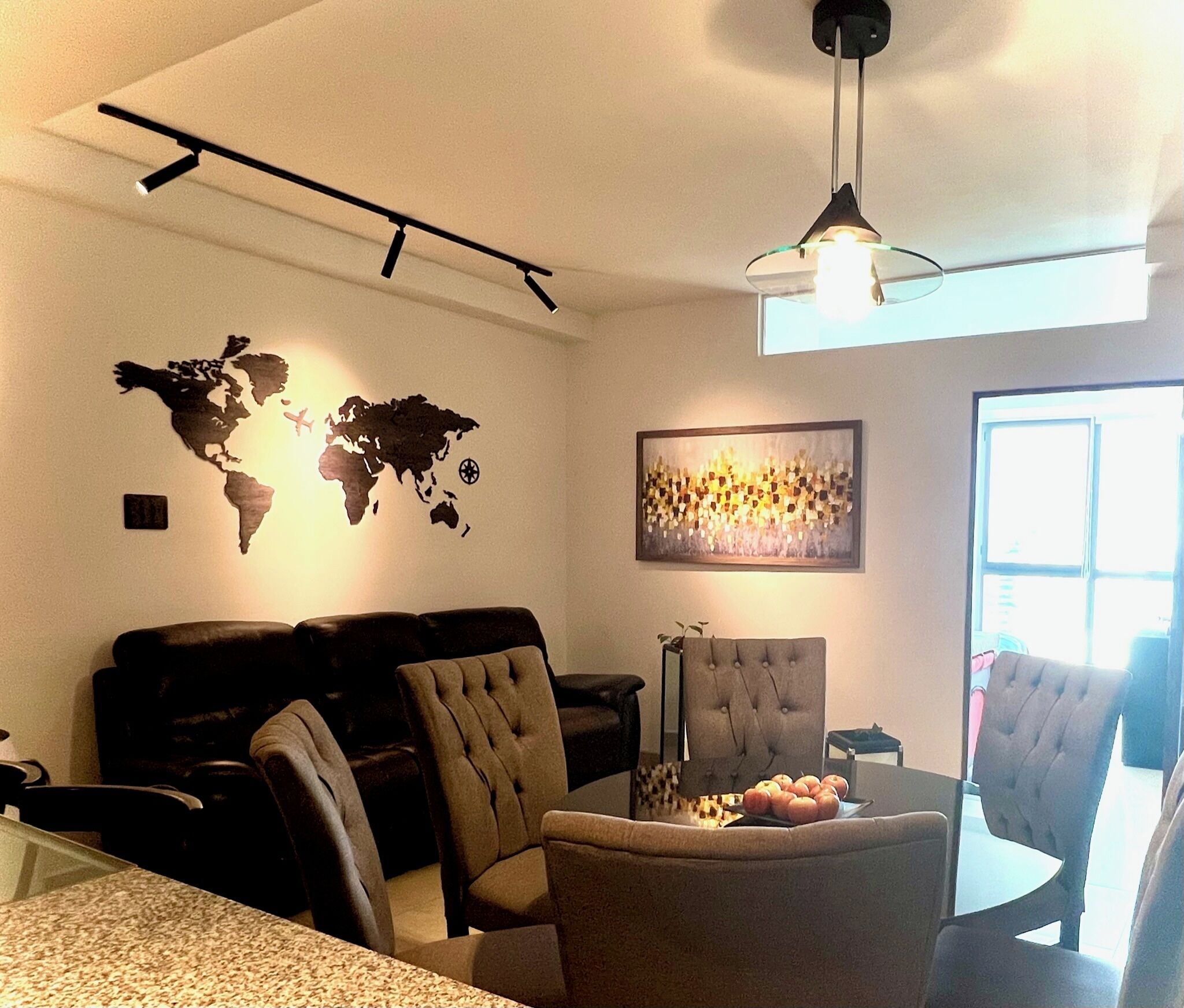 Un salon avec une carte du monde, un tableau abstrait encadré et un coin repas comprenant des chaises et une table.