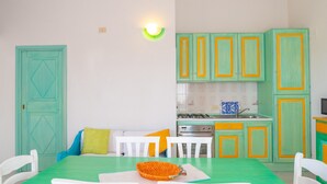 Una habitación con una mesa verde, sillas blancas, una cocina con armarios verdes y un salpicadero de azulejos azules y blancos.