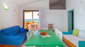 Una habitación con una mesa verde, un sofá azul, sillas blancas y vistas al exterior.
