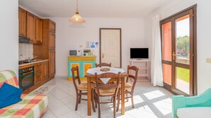 Un comedor con mesa y sillas, una cocina con armarios de madera, un televisor y un ventanal corredizo al exterior.