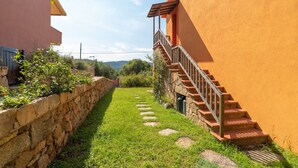Un muro de piedra, un sendero cubierto de hierba y una escalera que conduce a un edificio con fachada roja.