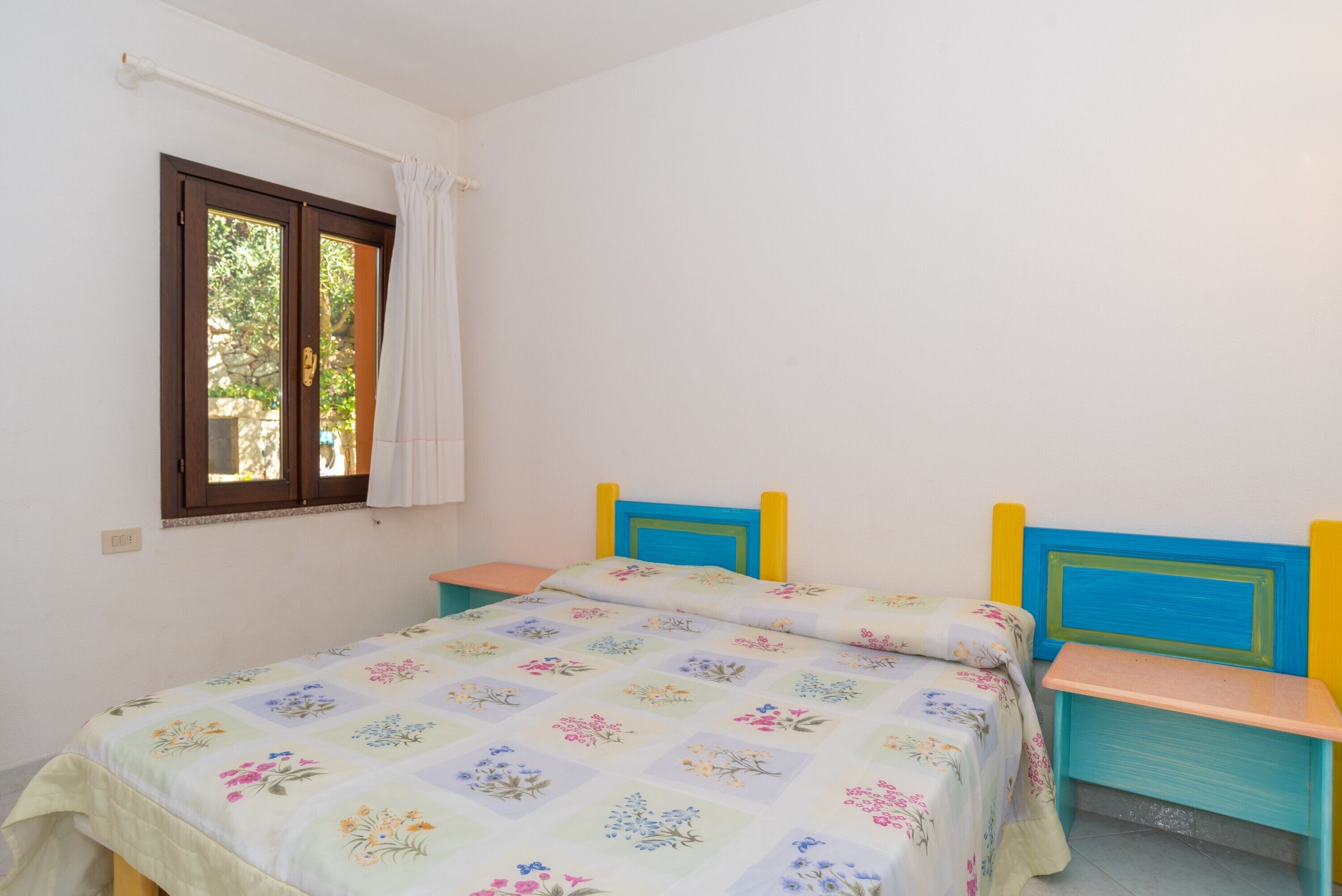 Une chambre à coucher avec un lit, une fenêtre avec des rideaux et une petite table.