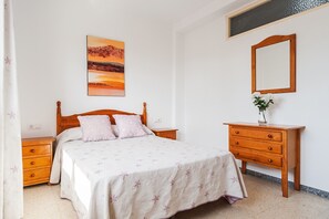 Um quarto com cama, mesa de cabeceira, penteadeira, espelho e um quadro na parede.