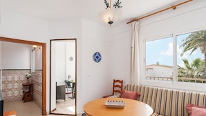 Ein Wohnzimmer mit einer Couch, einem Esstisch und Blick auf Palmen durch ein Fenster.