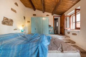 A bedroom with a bed, a wardrobe, a window, and a stone floor.