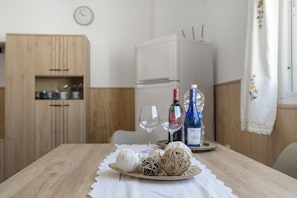 Mesa de jantar com toalha branca, duas taças de vinho, uma garrafa de vinho e objetos decorativos.