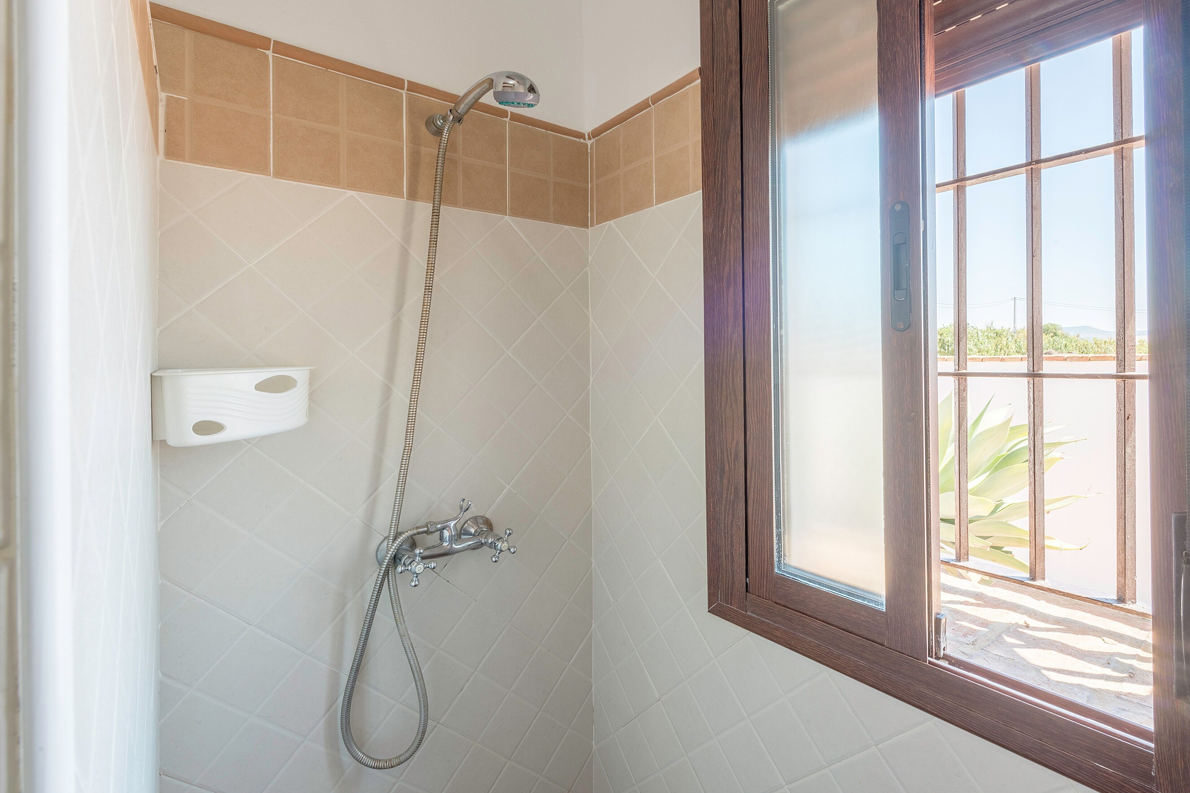 Une douche équipée d’un flexible, d’un pommeau de douche fixé au mur et d’une fenêtre donnant sur un paysage verdoyant.