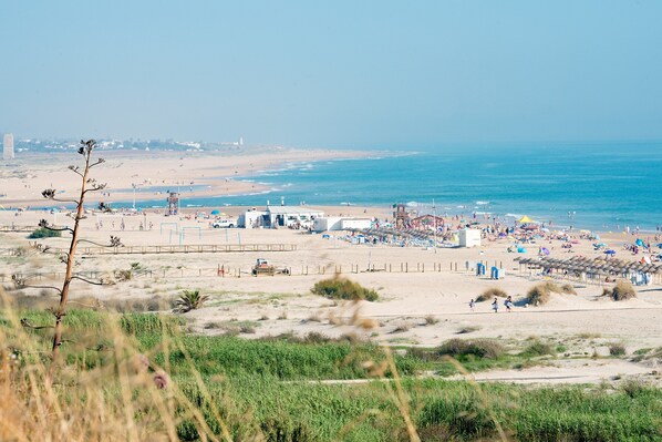 Une plage avec un poste de surveillance pour les sauveteurs, des parasols et des personnes qui se prélassent au soleil.