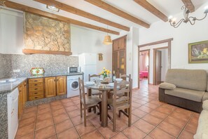 Une cuisine avec des meubles de rangement en bois, un mur en pierre, une table à manger avec des chaises et un canapé.