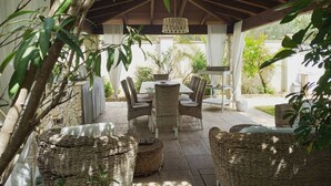 Une terrasse extérieure aménagée avec des meubles en osier, une table et un luminaire suspendu.