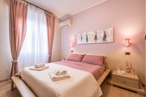 Een slaapkamer met een bed, nachtkastje, decoratieve wandkunst en gordijnen.