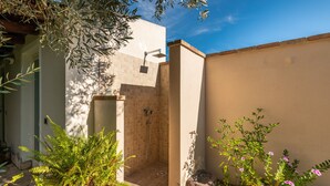 Un espace de douche extérieur abrité, doté d’un mur carrelé, d’une plante en pot et d’un chemin en pierre.