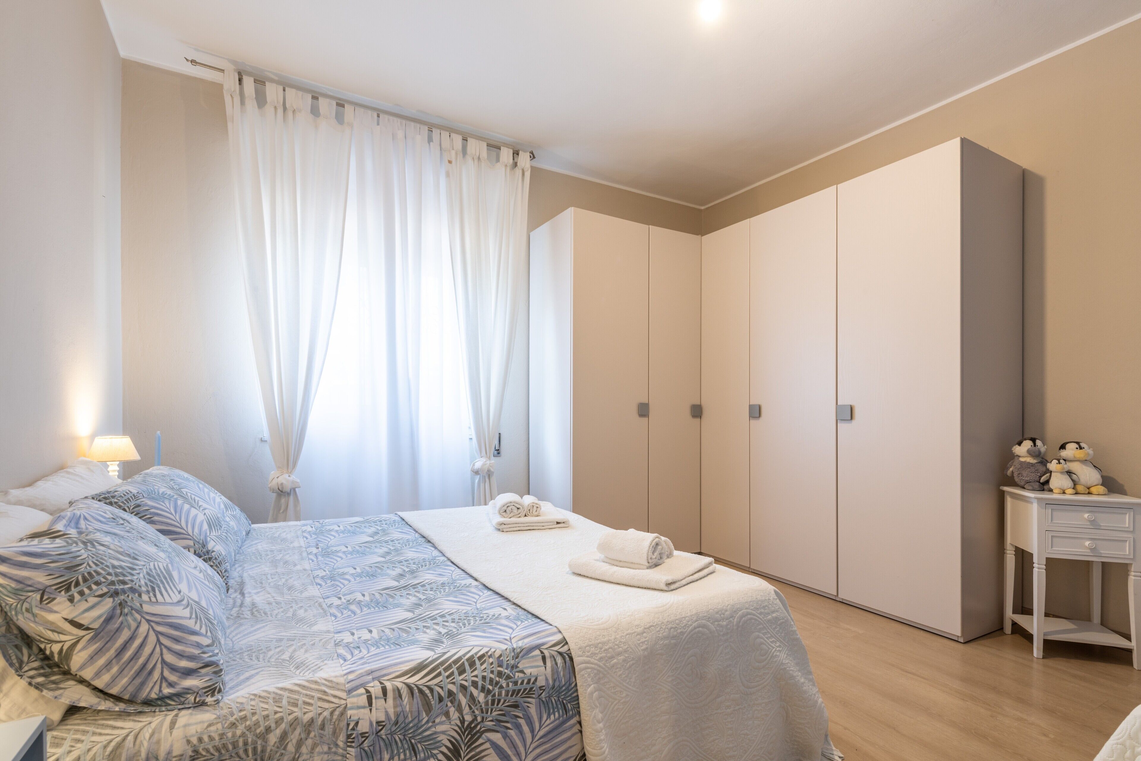 A bedroom with a bed, a nightstand, a wardrobe, and a window with curtains.
