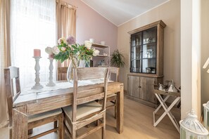 A wooden dining table with chairs, a vase with flowers, a cabinet with glass doors, and a small table with a lantern.