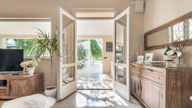 Un couloir avec un meuble en bois, un téléviseur, une plante en pot et une porte-fenêtre donnant sur l’extérieur.