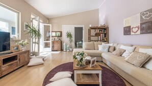 Un salon avec un canapé, une table basse et un téléviseur. On y trouve également une bibliothèque et une plante.