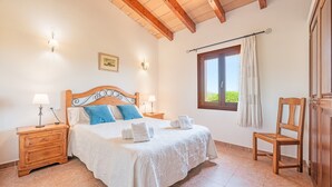 Un dormitorio con una cama de madera, dos mesitas de noche con lámparas, una ventana con cortinas y una silla de madera.