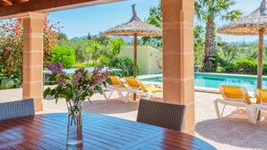Un espacio exterior techado con piscina, sillas de descanso y una mesa con un jarrón de flores.