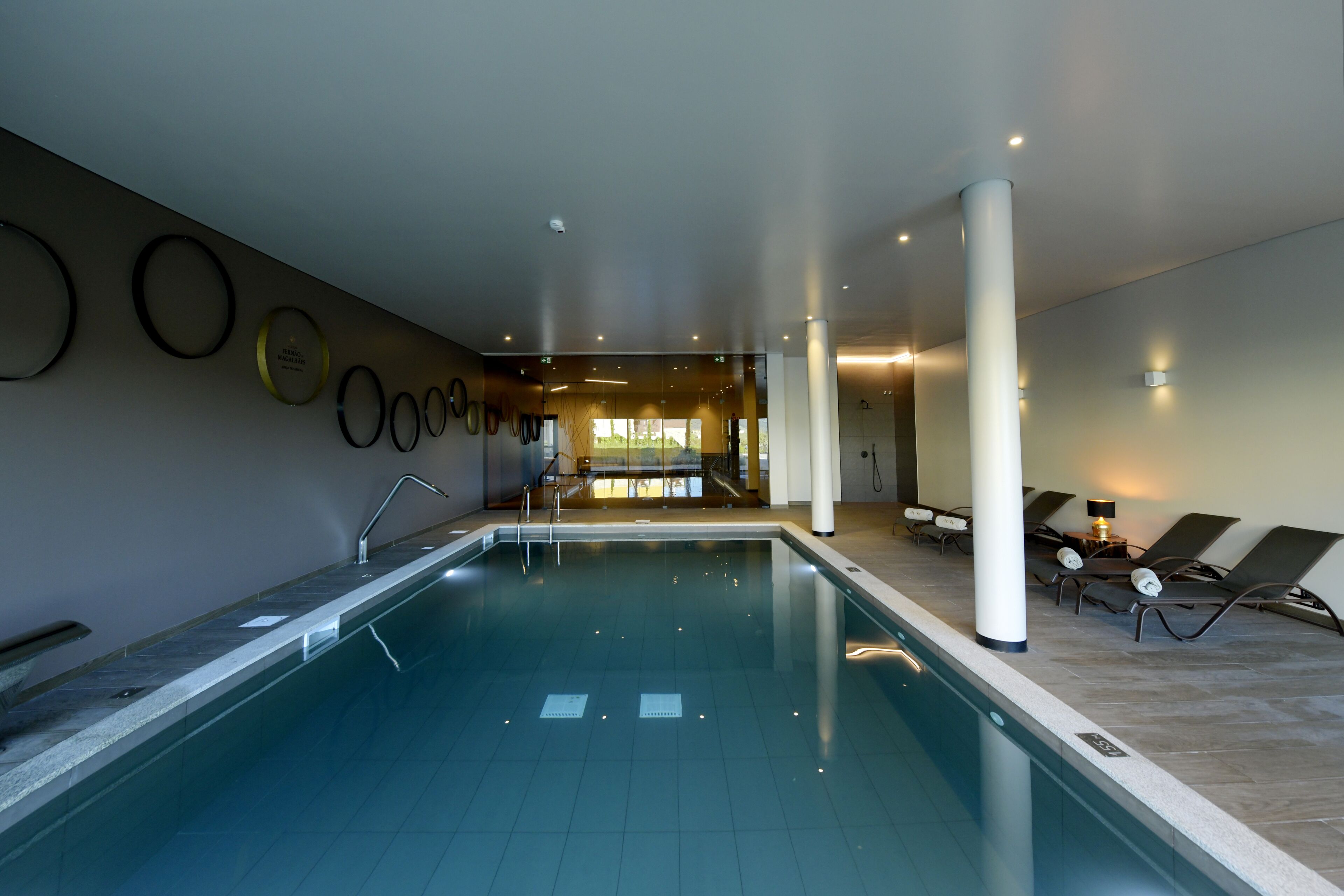 An indoor swimming pool with a clear view of the pool area, a reception desk, and lounge chairs.