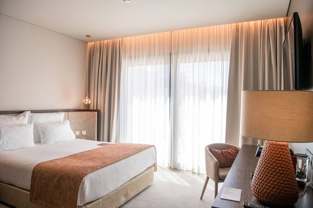Une chambre d’hôtel avec un grand lit, un bureau avec une lampe et un téléviseur fixé au mur.