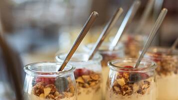 Une table en bois sur laquelle sont disposés des pots en verre contenant un dessert crémeux, garni de granola et de fruits rouges, accompagnés de cuillères en métal.