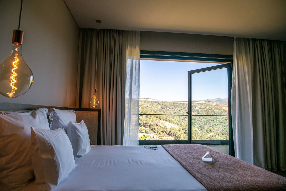 Une chambre d’hôtel avec un lit, une vue sur la campagne et un luminaire suspendu.