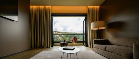Una habitación de hotel moderna con un ventanal grande, un sofá, una mesa de centro y una lámpara.