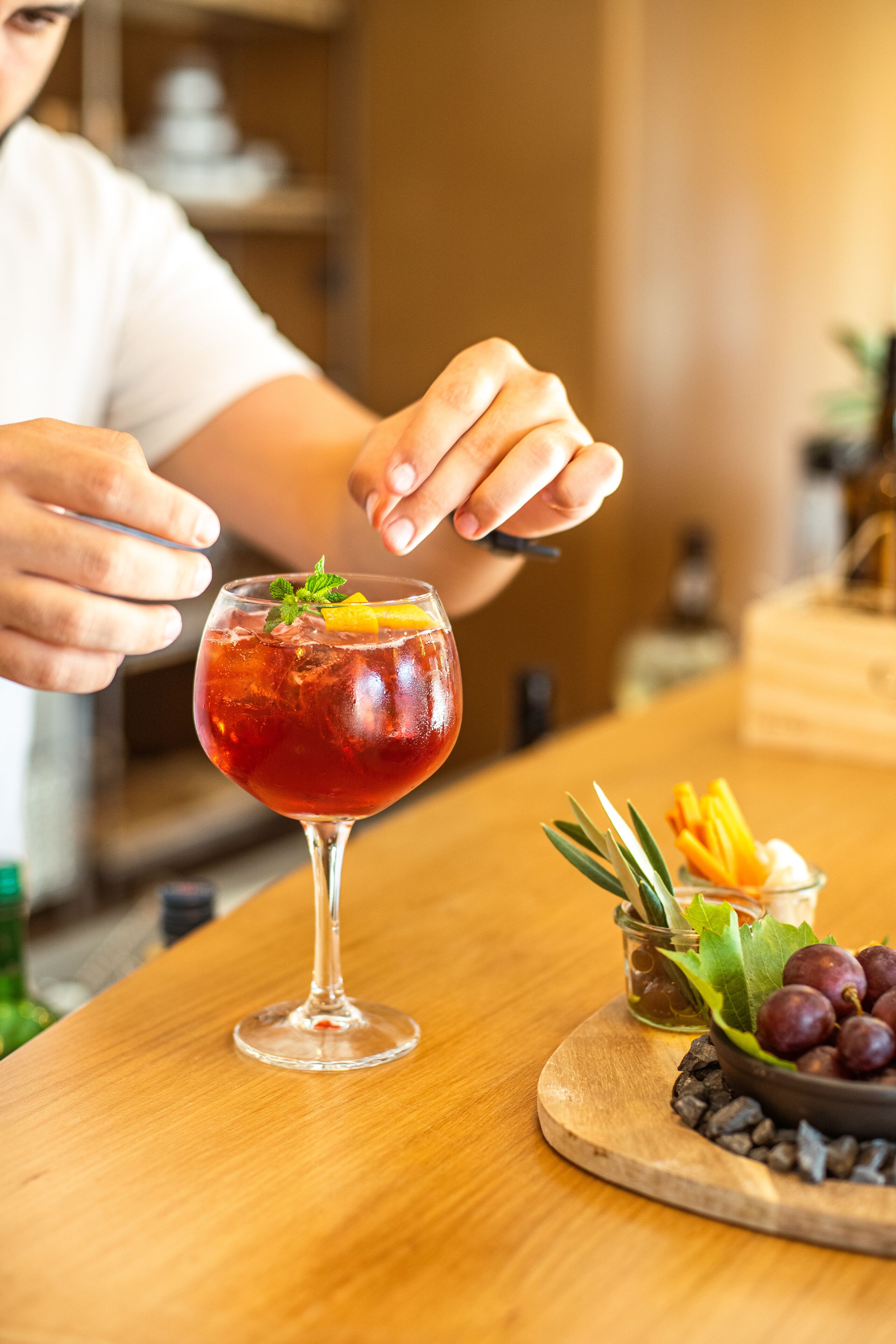A person garnishing a cocktail with a mint leaf and orange slice.
