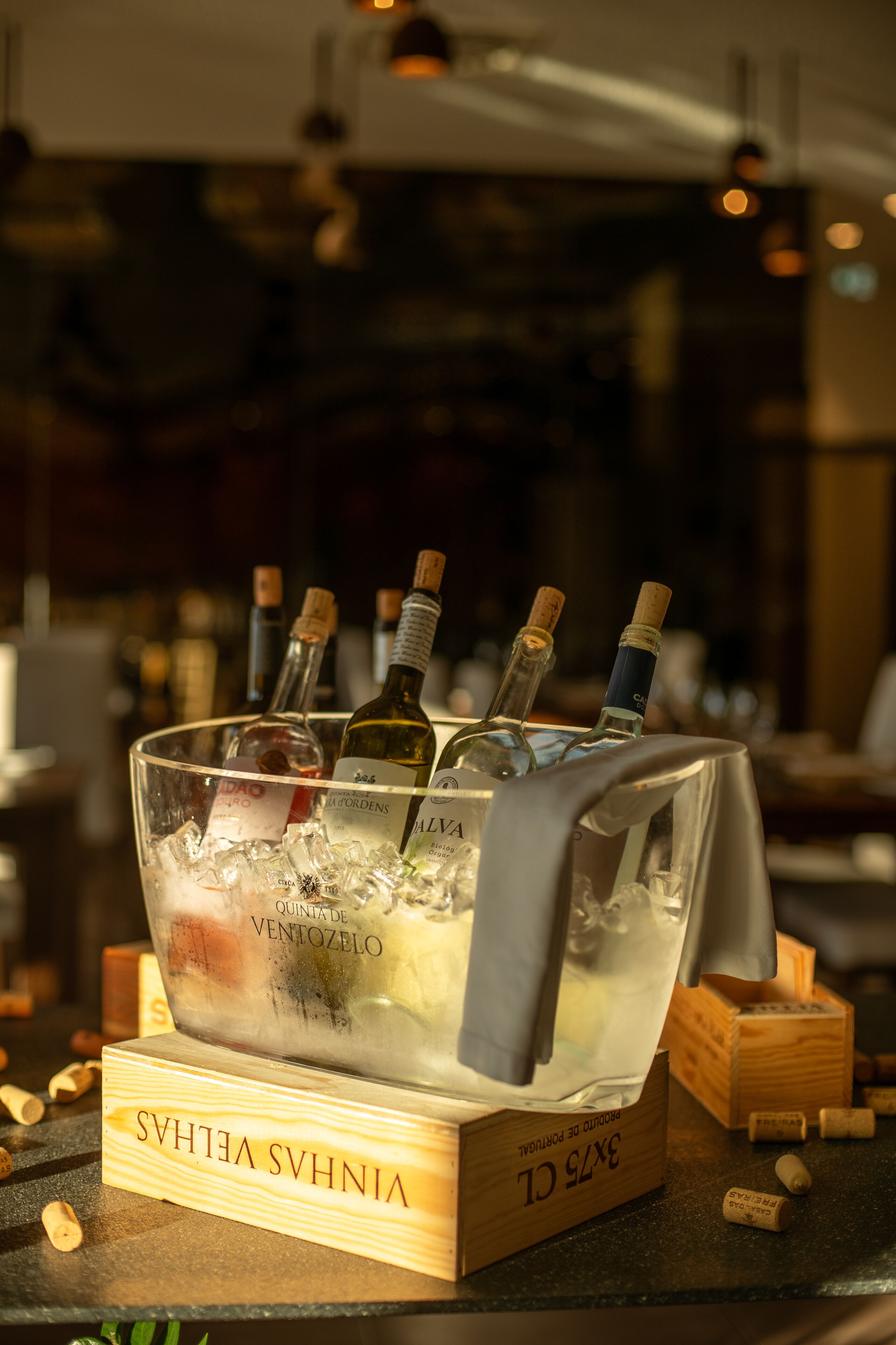 A bar area with a glass container holding bottles of wine and corks, surrounded by wooden blocks with text.