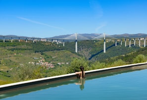 Una persona relajándose en una piscina con vistas a un puente y un paisaje montañoso.