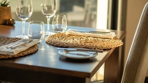 Une table à manger dressée avec des assiettes, des couverts et des verres, donnant sur un paysage urbain à travers une fenêtre.