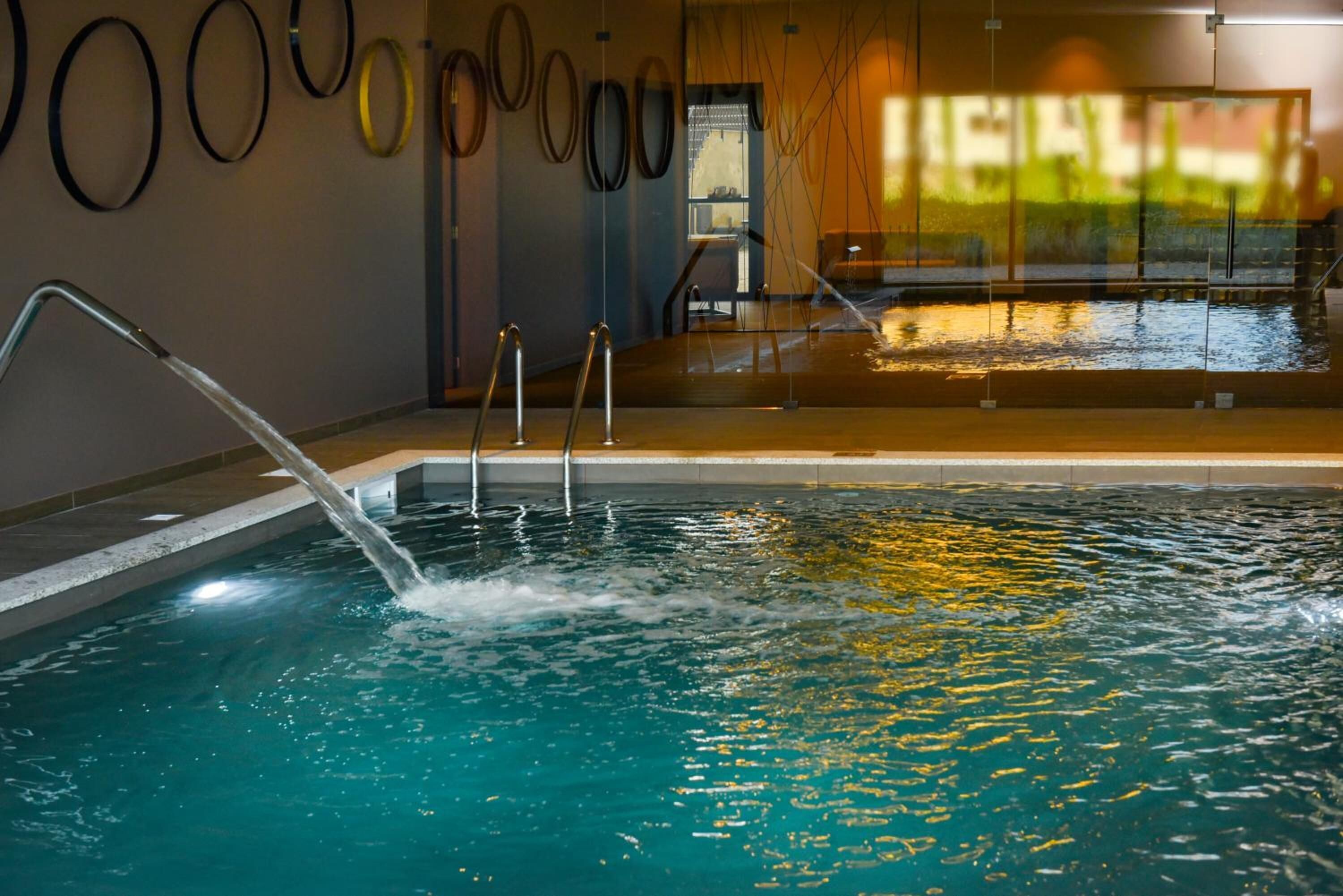 An indoor swimming pool with clear water, metal railings, and a view of the outdoors through a large window.