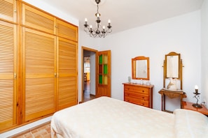 A bedroom with a large bed, wooden wardrobe, dresser, and a mirror.