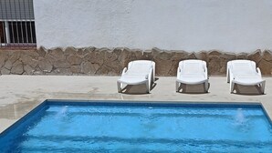 Une piscine à l’eau d’un bleu cristallin, trois chaises longues blanches et un bâtiment blanc doté d’un socle en pierre.