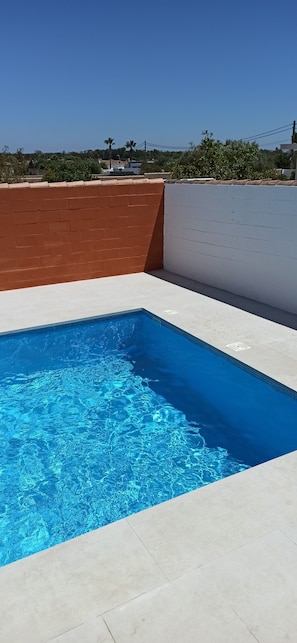 A rectangular swimming pool with clear blue water, surrounded by a white and brown wall, and a clear sky in the background.
