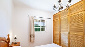 Une chambre à coucher avec un lit en bois, une table de chevet avec une lampe, une fenêtre avec des rideaux et une armoire en bois.