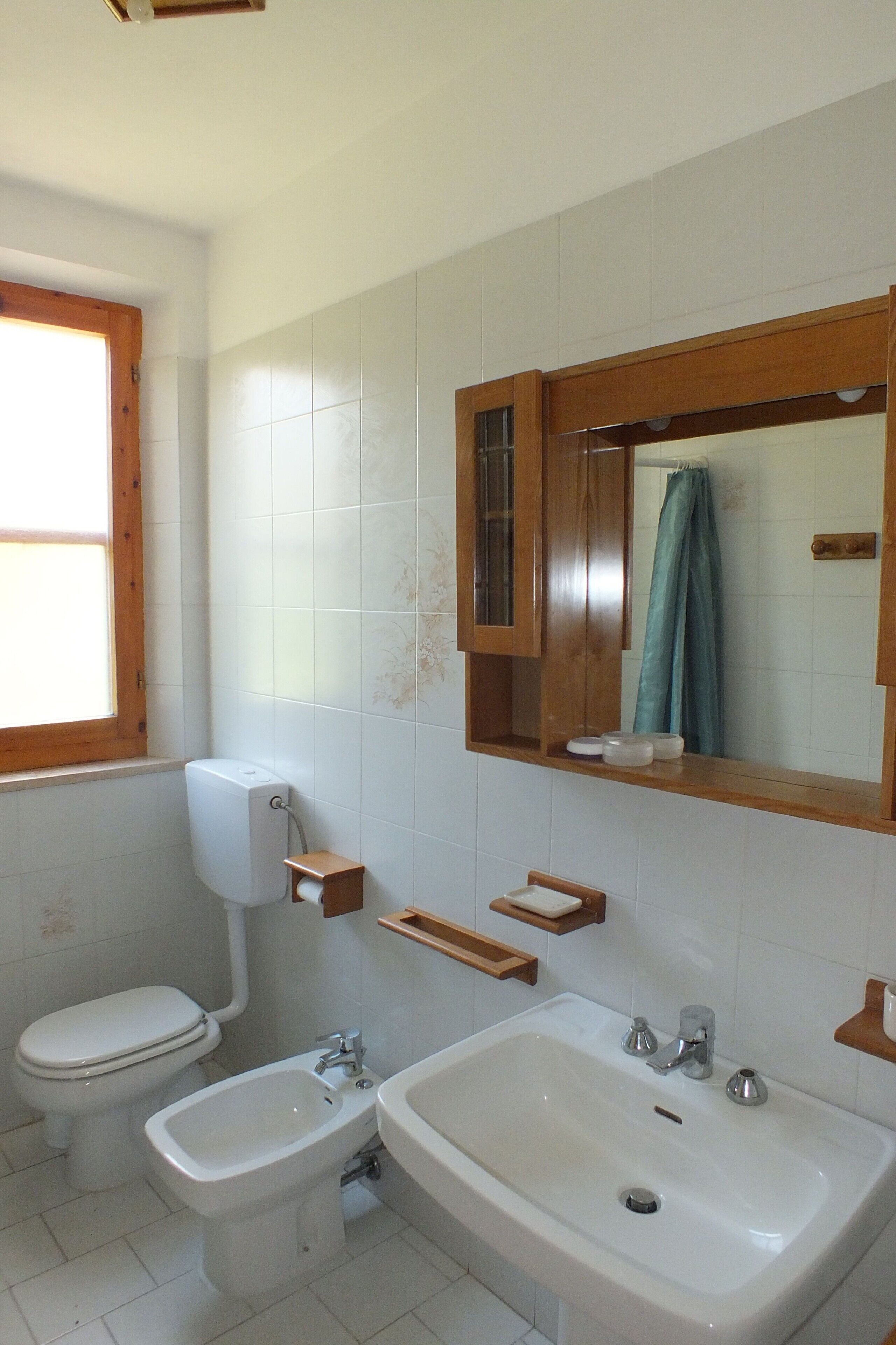 Een badkamer met toilet, bidet, wastafel en een houten medicijnkastje.