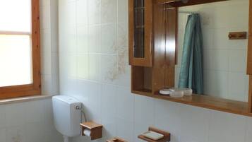 Een badkamer met toilet, bidet, wastafel en een houten medicijnkastje.