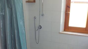 A bathroom with a shower, toilet, and a window.