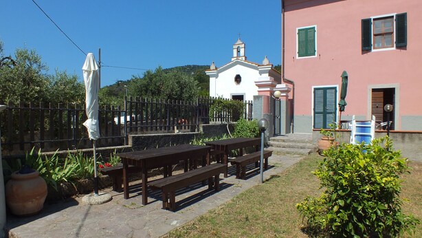 A courtyard with outdoor seating, a white building with a bell tower, and a pink building with shutters.