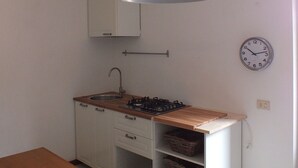 A kitchen with a wooden countertop, a gas stove, a white cabinet, a hanging light fixture, and a wall clock.