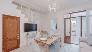 Een moderne woonkamer met een houten eettafel, witte stoelen, een televisie en een trap.