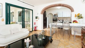 A living room with a white sofa, a black coffee table, and a dining area with a table and chairs. - Rustic Villa, Air Conditioning and Beautiful Garden (Orosei)