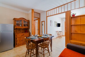 Un coin repas avec une table en bois dressée pour quatre personnes, un réfrigérateur et un meuble avec des portes en verre.
