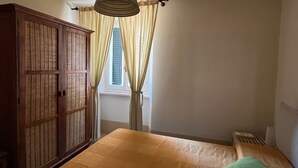 A bedroom with a bed, a wardrobe, a hanging light fixture, and a window with curtains.