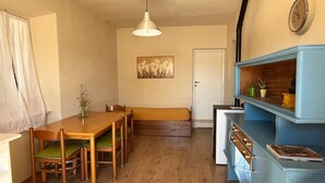 A dining area with a wooden table and chairs, a bench, a wall-mounted clock, and a blue cabinet with shelves.
