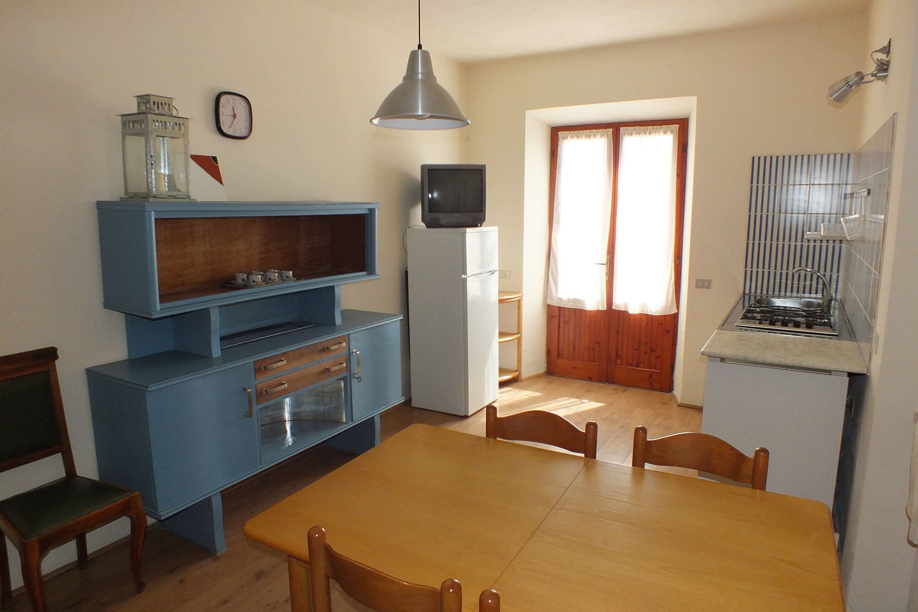 Eine kleine Küche mit Esstisch, Stühlen, Kühlschrank, Herd und einem blauen Schrank.